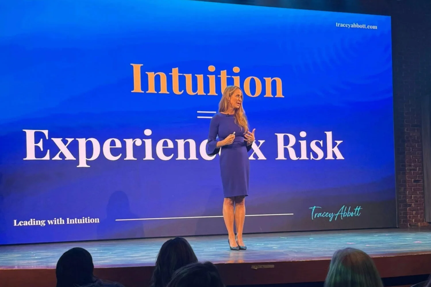 Tracey Abbott speaking on stage with the equation "Intuition = Experience × Risk" displayed behind her.
